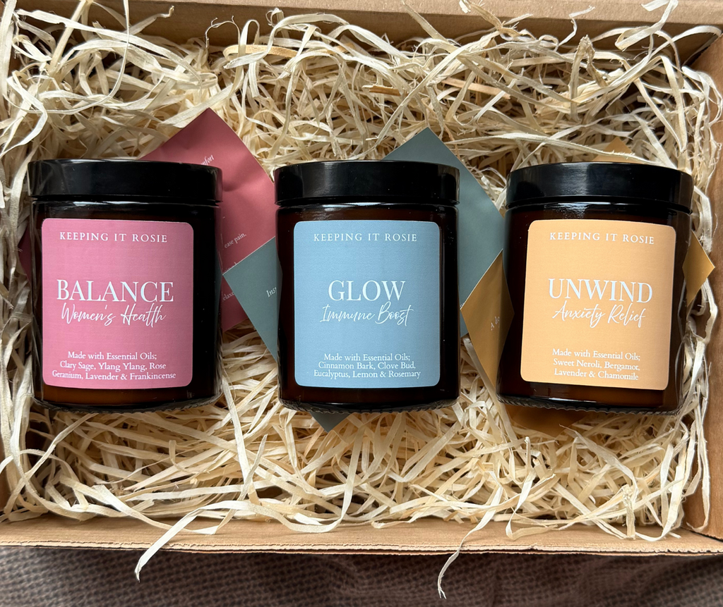 Three candles in a decorative box with 'Keeping It Rosie' branding. Wellness blend essential oil candles